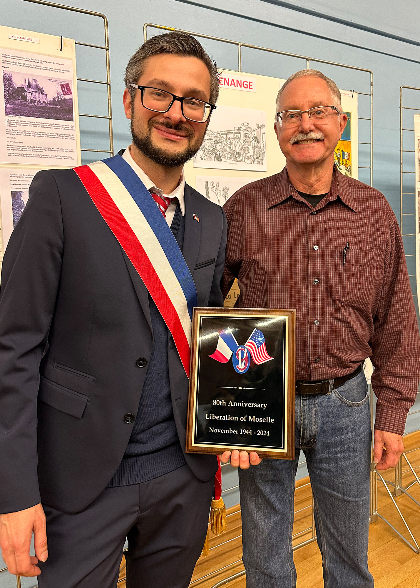 Guénange Mayor Pierre Tacconi accepts a plaque commemorating the 80th Anniversary of the Liberation of Moselle from Mike Flora. The plaque was a gift from the 95th Division Legacy Association and the 95th Division Foundation.