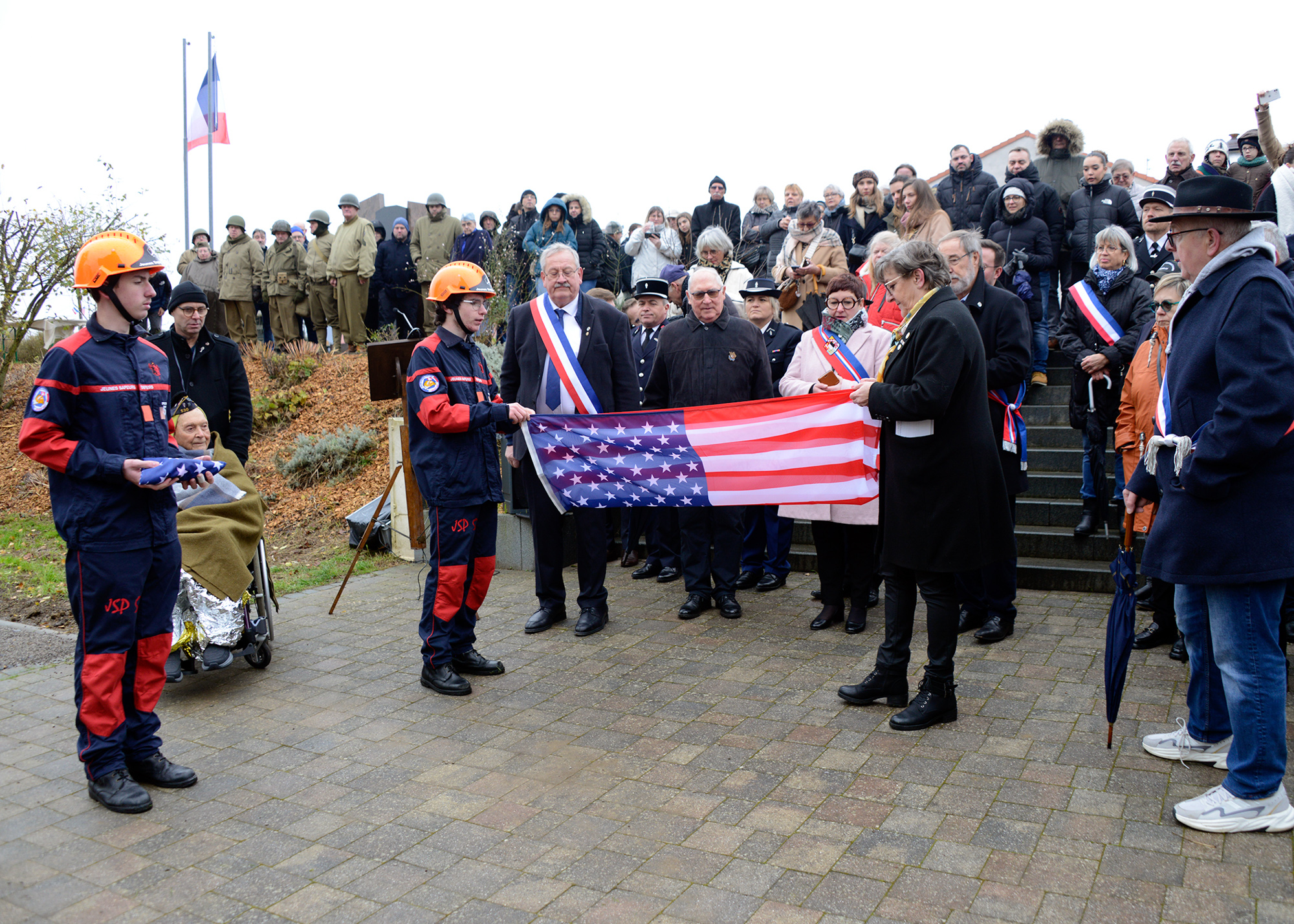 A young firefighter assists Valérie Muller from the American Battle Monument Commission fold an American flag. Ms. Muller then presented the flag to Ceo Bauer.