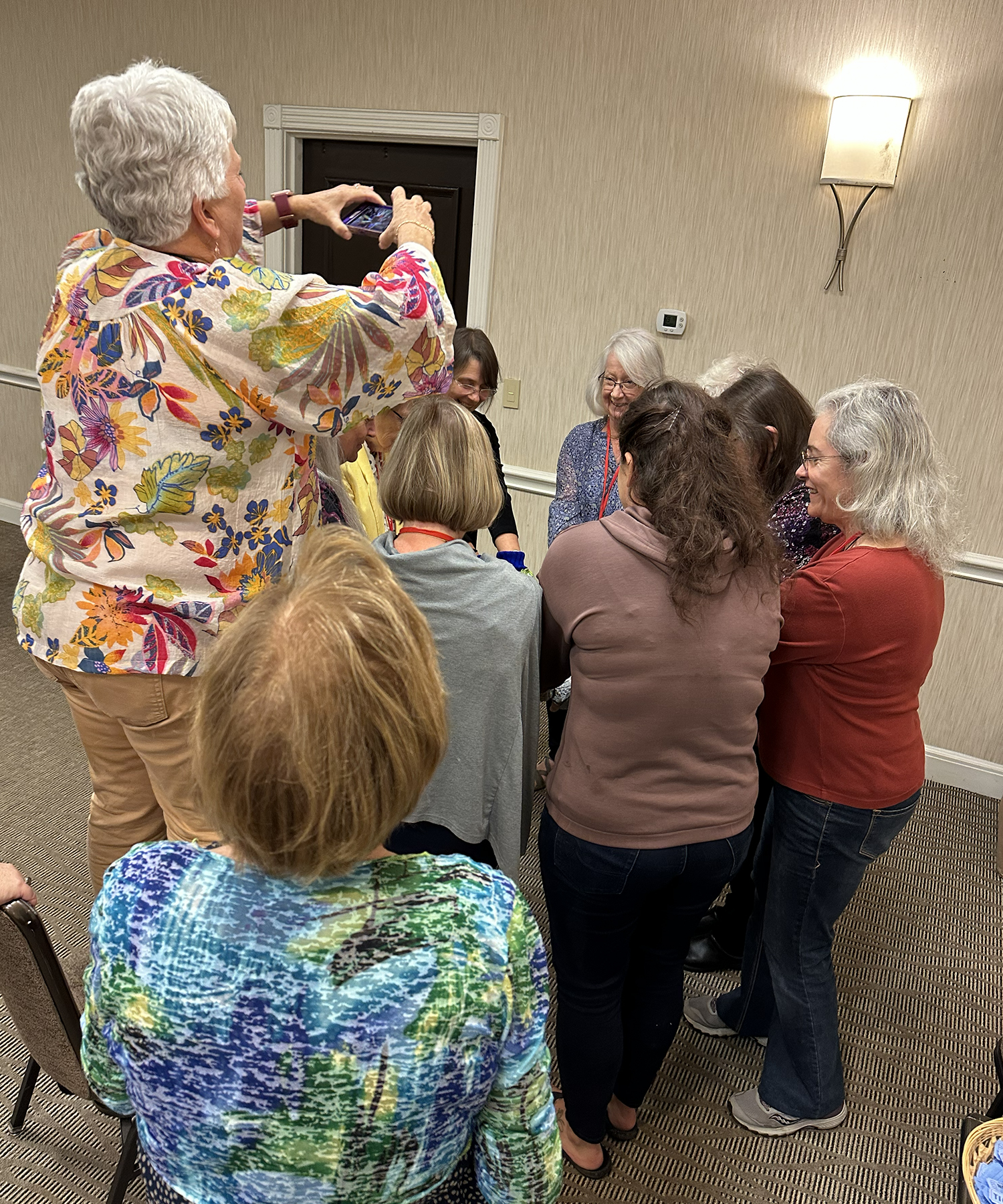 Billie Bauer climbed upon a chair to get a better angle for a photo of the Victory Belles proudly displaying their raffle prize hand warmers donated by Françoise Leclercq.