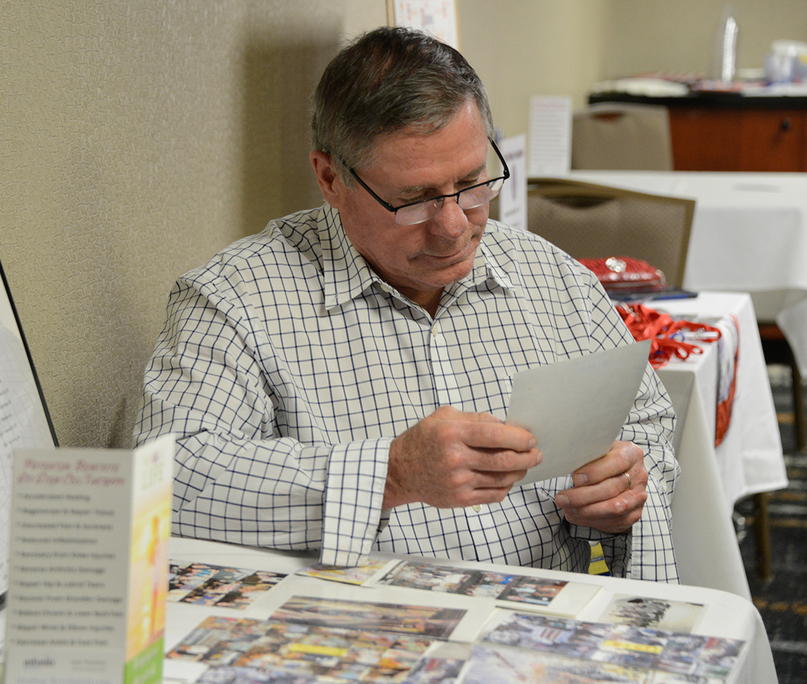In the Hospitality Room, Carl Urbon looks at a collection of photos from past reunions. Often attendees bring photos to share at the reunions.